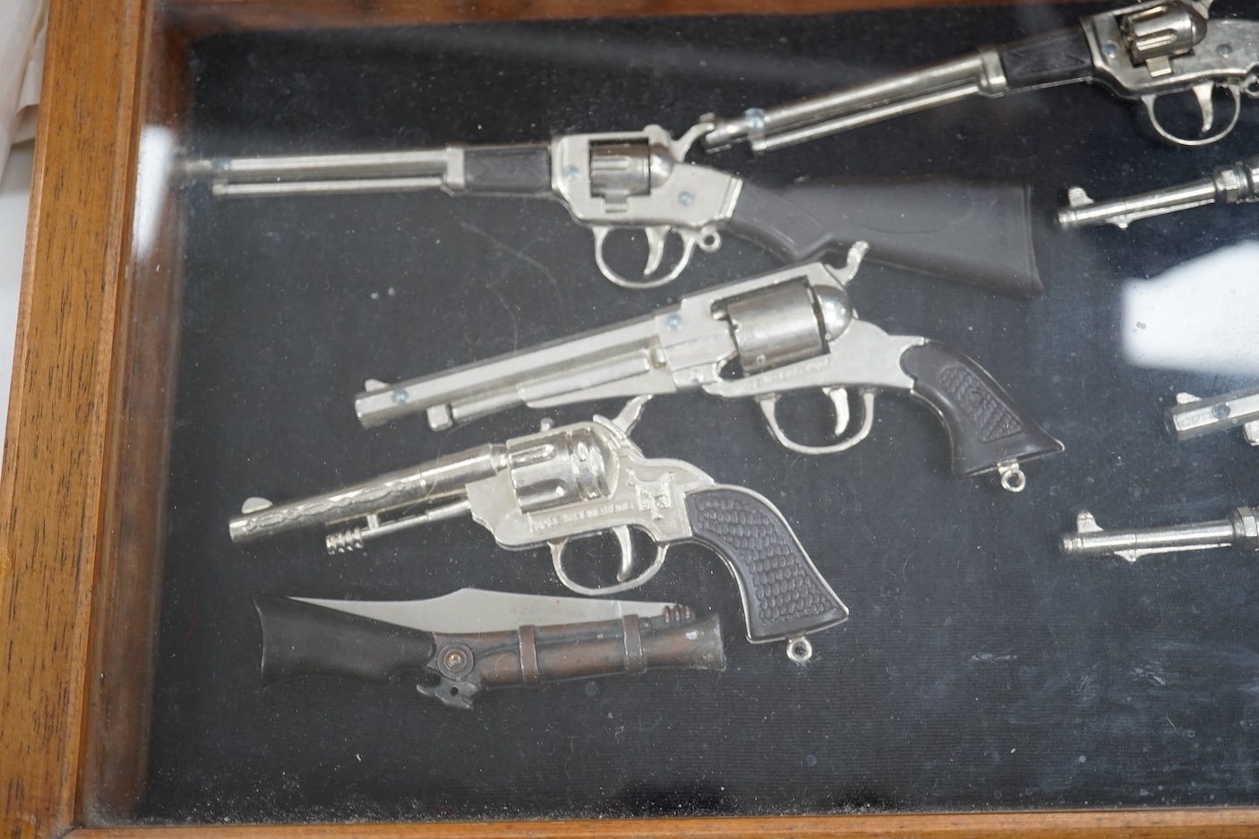 Sundry items comprising a small figured walnut table top collectors cabinet, a display case containing miniature rifles and pistols, a collection of copper and brass miniature RMS nameplates